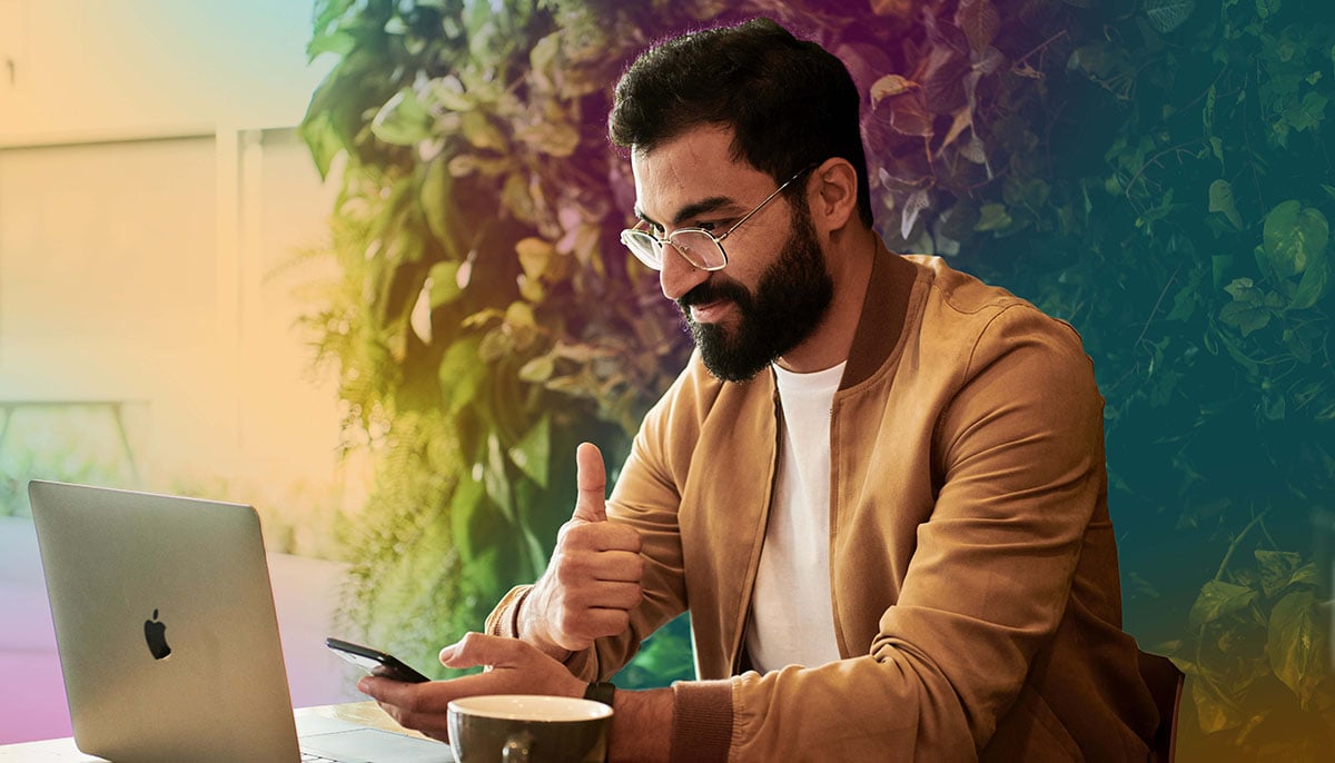 Man vid laptop och mobil i handen